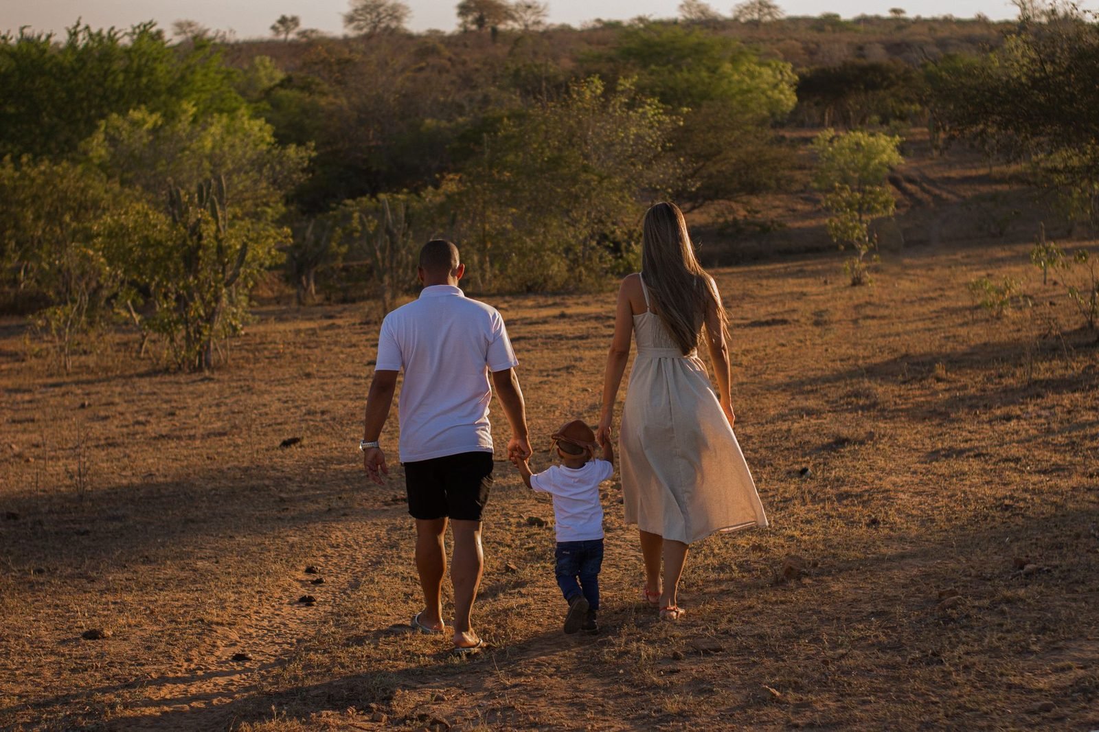 Pais de mãos dadas com filho pequeno em momento afetuoso ao entardecer
