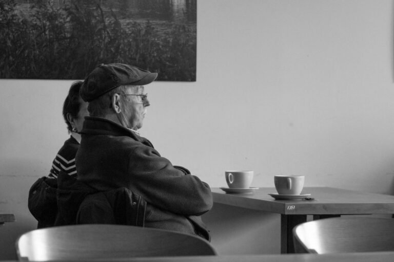 Duas vizinhas idosas conversam amigavelmente enquanto tomam café na mesa da cozinha, luz natural.
